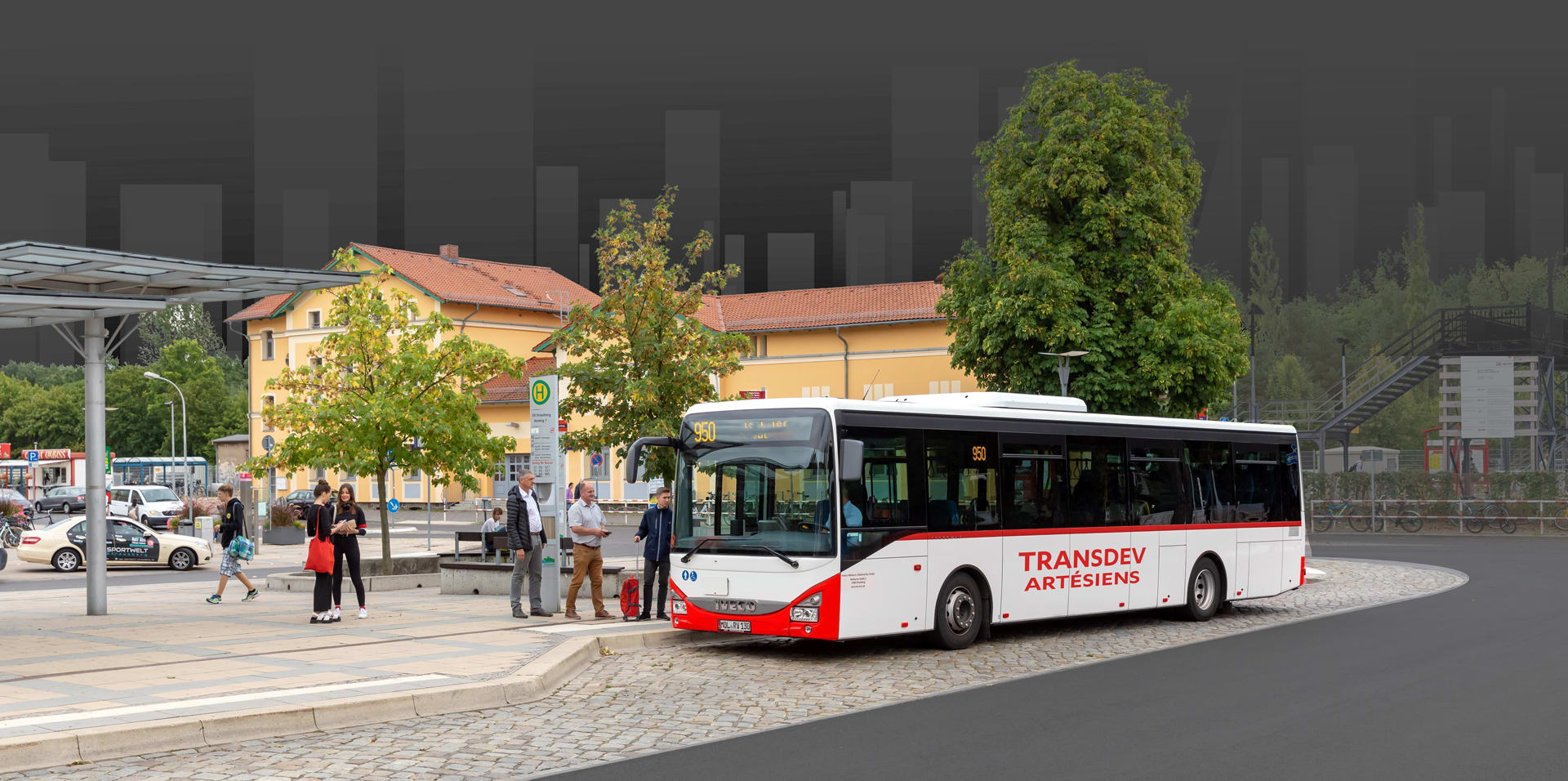 La photo montre un arrêt de bus où des personnes s'apprêtent à monter dans un bus Transdev