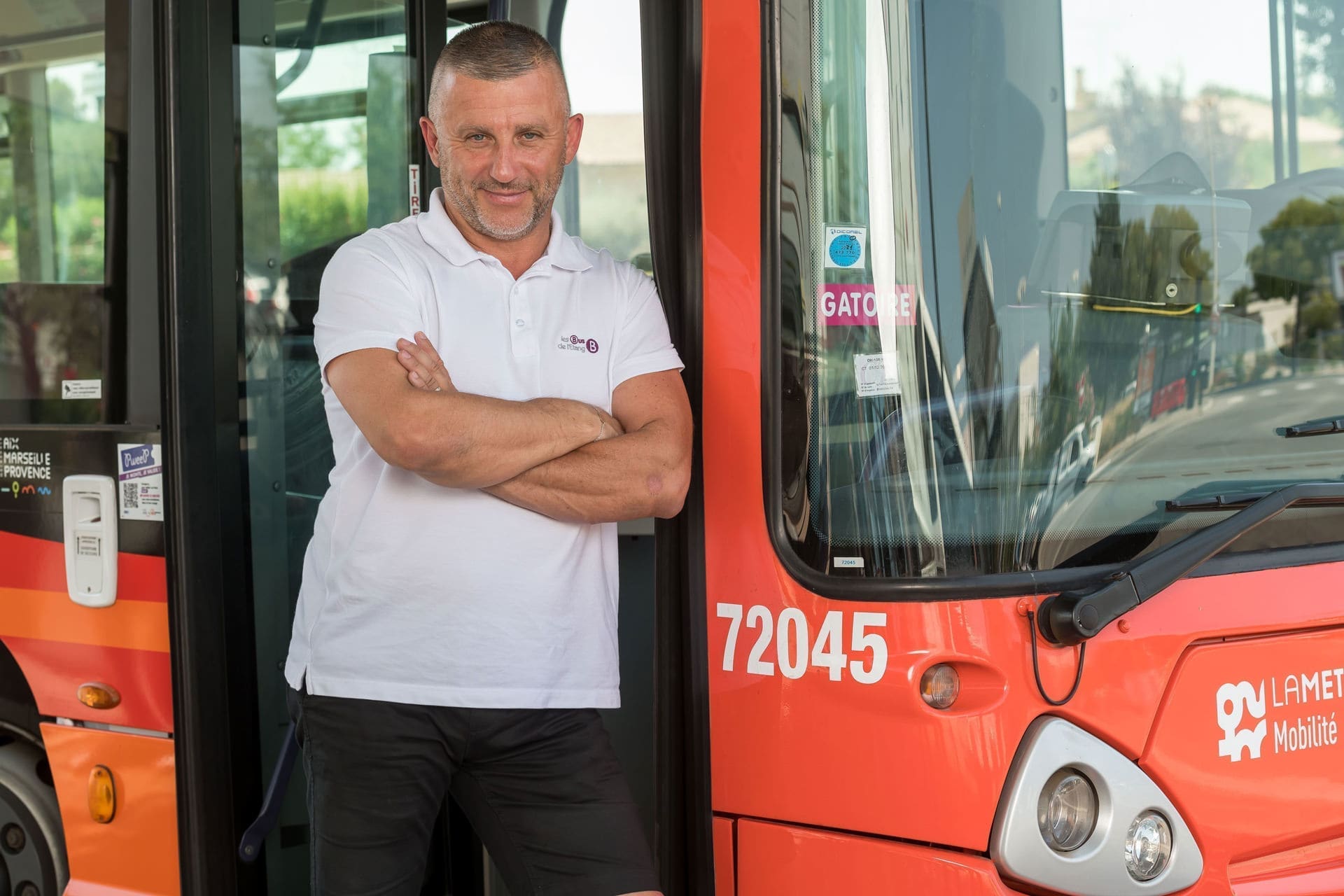 Photo d'un conducteur de bus souriant et appuyé sur son devant son véhicule